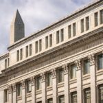 The historic Federal Reserve building with its imposing marble columns under a clear blue sky
