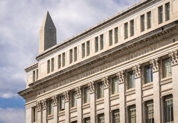 The historic Federal Reserve building with its imposing marble columns under a clear blue sky