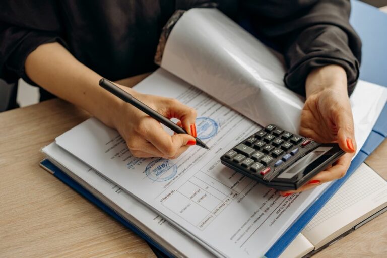 An office desk with financial documents, calculators, and bookkeeping ledgers representing the difference between bookkeeping and accounting.