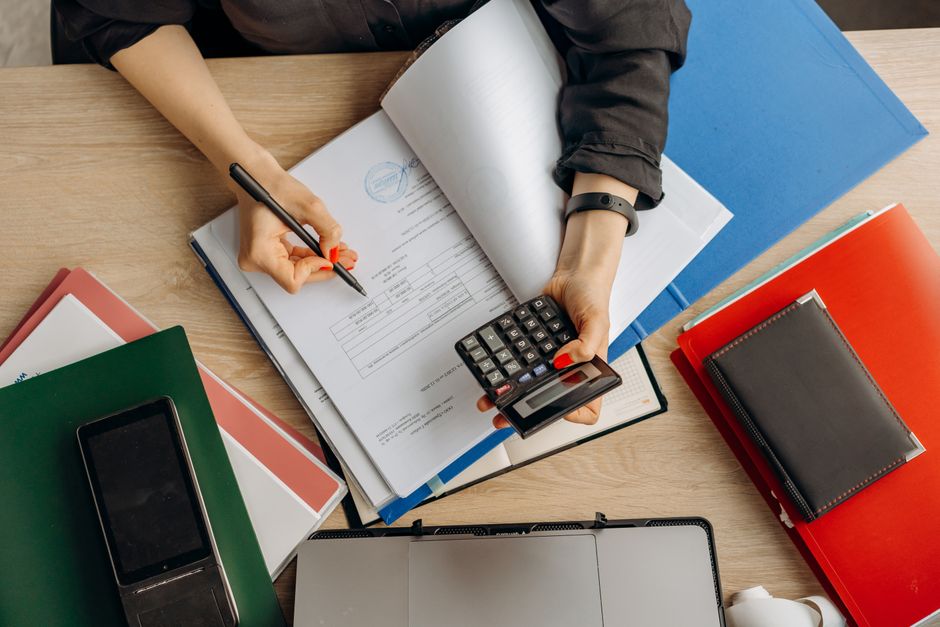 A professional reviewing general ledger transactions on a dual-screen monitor with financial charts.
