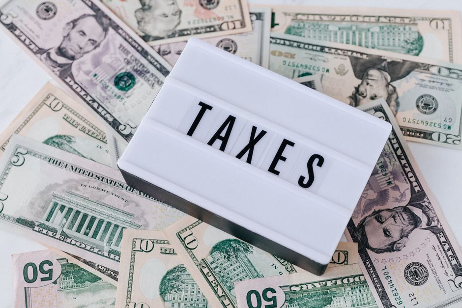 A calculator, tax documents, and US dollar bills on a desk representing common indirect taxes in the USA.
