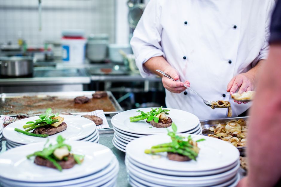 A busy commercial restaurant kitchen with chefs preparing dishes.