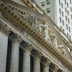 The exterior of the New York Stock Exchange building under a cloudy sky.