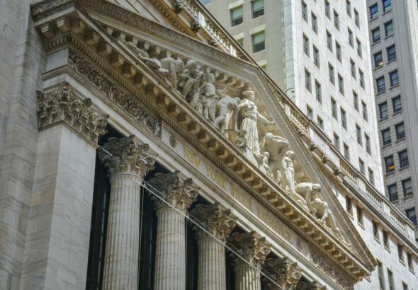 The exterior of the New York Stock Exchange building under a cloudy sky.