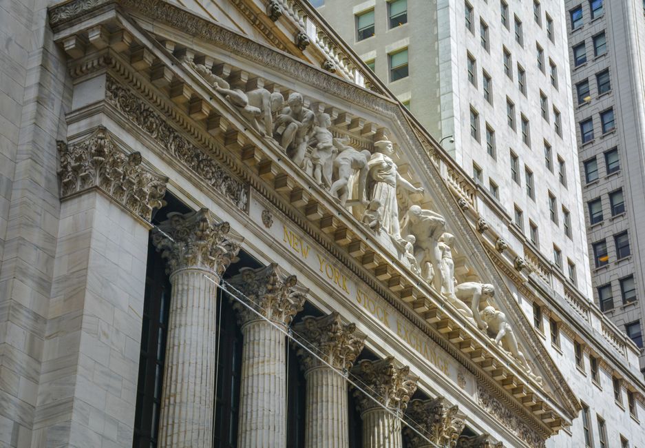 The exterior of the New York Stock Exchange building under a cloudy sky.