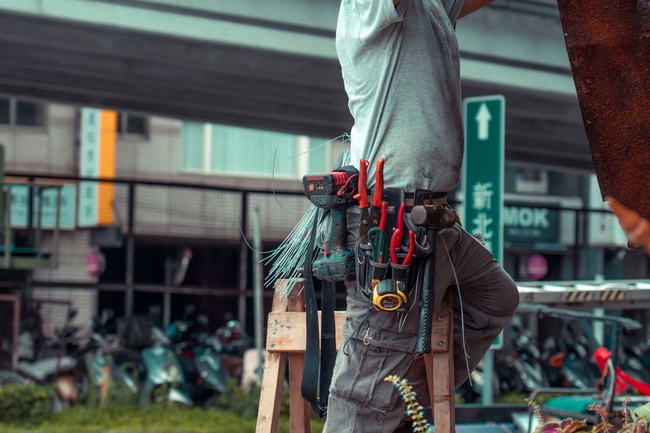 A handyman with a tool belt inspecting repair equipment on a work site.